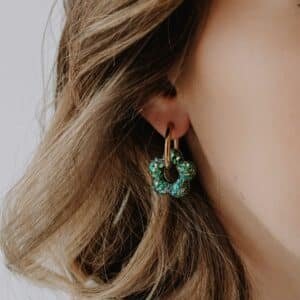 Créoles Oia Artemisia dorées avec fleur en résine verte portées à l’oreille