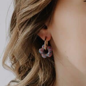 Créoles Oia Cléome dorées avec fleurs en résine rose et vert posées sur fond clair