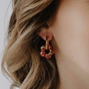 Créoles Oia Coquelicot dorées avec fleur en résine rouge orangé posées sur fond clair