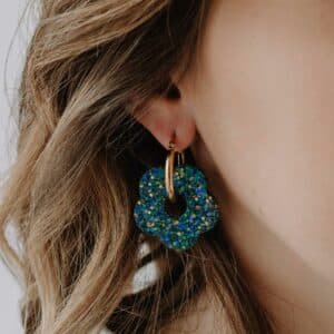 Photo des Grandes Créoles Oia Bleuet, boucles dorées avec fleurs bleues en résine mate, fabrication artisanale en Bretagne