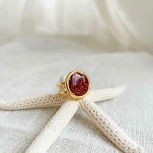 Bague Sonora rubis dorée avec pierre rouge étincelante posée sur une surface claire dans une lumière douce et naturelle