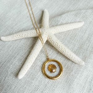 Collier Cancun avec pendentif rond doré et inclusion coquillage sur fond clair, présenté sur une étoile de mer.