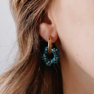 Créoles Oia Luz dorées avec fleur en résine bleu aqua posées sur fond clair