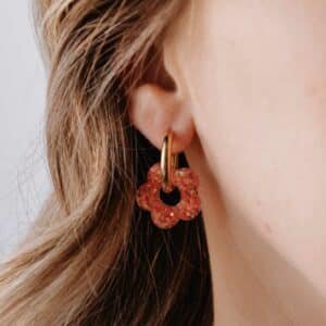 Créoles Oia Solandra dorées avec fleur en résine orangée portées à l’oreille