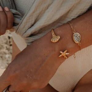 Bracelet Carmen doré à l’or fin 24k, orné d’un médaillon ovale en résine transparente incrustée d’éclats argentés, porté au poignet.