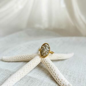 bague carmen en or 18k aux éclats lumineux posée sur une étoile de mer blanche sur un tissu beige clair et texturé