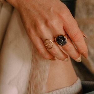 Bagues artisanales Atelier R portées à la main, modèle résine noire et modèle motif floral doré.
