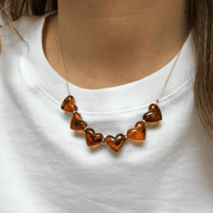 Collier Love - Ambre avec cœurs en résine marbrée ambre montés sur une chaîne dorée fine, porté autour du cou.