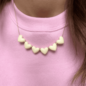 Collier Love - Crème avec cœurs en résine crème sur chaîne fine dorée porté sur pull rose
